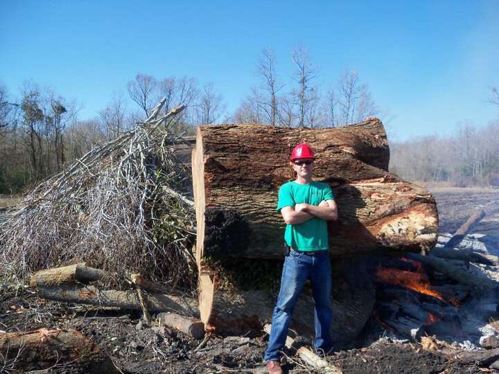 Man from Arbor Tech Tree Service standing confidently beside a large, freshly removed tree stump.